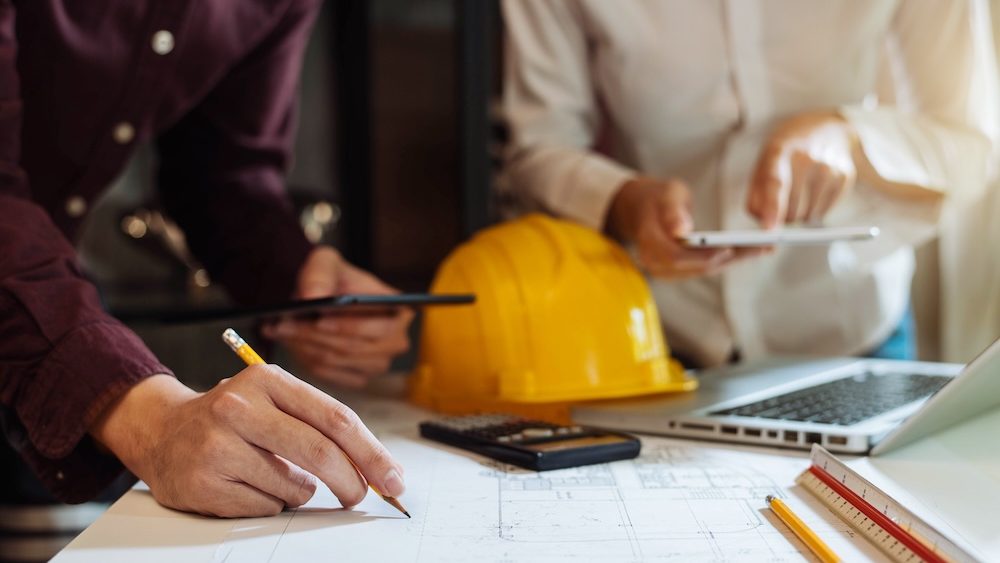 Businessman working as a team discussing data working and tablet, laptop with on on architectural project at construction site at desk in office.