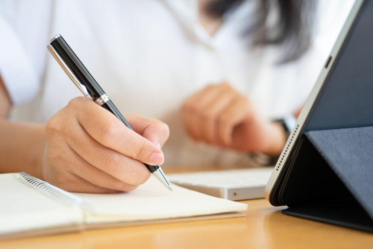 Close shot of businesswoman hands holding a pen writing something on the paper on the foreground in office. Recording concept