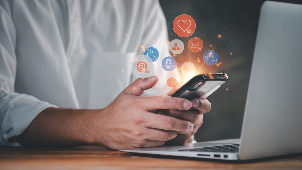 Social media interactions on mobile phone, concept with notification icons of like, message, email, comment and star above smartphone screen, person hands holding device, internet digital marketing