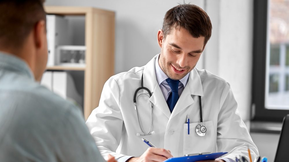 medicine, healthcare and people concept - doctor with clipboard talking to male patient at medical office in hospital
