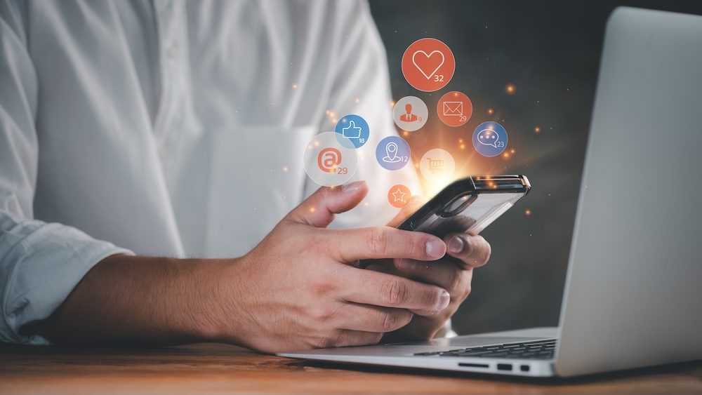 Social media interactions on mobile phone, concept with notification icons of like, message, email, comment and star above smartphone screen, person hands holding device, internet digital marketing